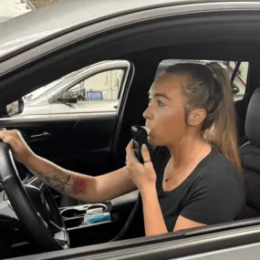 A driver demonstrates how to use an ignition interlock device by providing a breath sample before starting the vehicle.