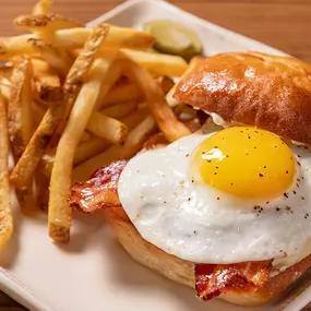 Farmhouse Burger with applewood smoked bacon, fried sunny egg, American cheese, and roasted garlic aioli on a potato bun.