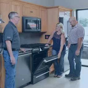 A showroom featuring a variety of high-end kitchen appliances. A sales associate is demonstrating the features of an oven to a couple. The clean and modern setup suggests an emphasis on quality products and customer experience.