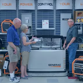 A store showcasing Generac generators. A sales associate is explaining the features of a large home generator to a senior couple. The display includes multiple portable power products, emphasizing the variety and expertise available at the store.