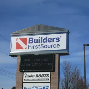 A roadside sign for Builders FirstSource, featuring a bold red and blue logo with 