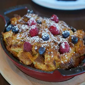 Cast Iron French Toast with rustic challah, berries, powdered sugar, and maple syrup in a cast iron (Weekend Brunch Menu).