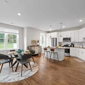 A dining area leads into an open kitchen with hardwood-style flooring near a large window.