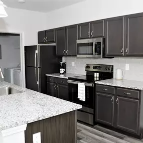 A kitchen with granite countertop, hardwood-style flooring, and pendant lights at Sugar Creek Apartments.