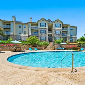 A swimming pool with umbrellas and lounge chairs near The Legends on the Park apartment buildings.