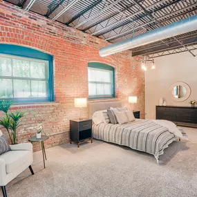 A bedroom with industrial brick walls and two large windows at Wireworks Lofts in the Square.