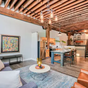 A living room with wooden ceiling panels near a kitchen with a small staircase leading to a lofted area at Wireworks Lofts in the Square.