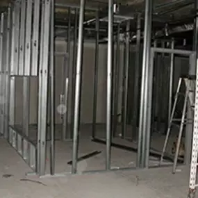 An interior view of a building under construction with exposed steel framing and scaffolding. The unfinished space shows the framework for walls and ceilings, representing the early stages of a structural build or restoration project.