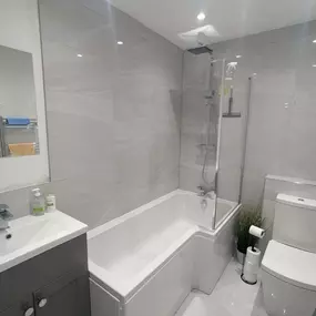 Modern bathroom with a grey vanity, white bath, and large-format tiles.