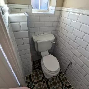 Compact toilet space with white subway tiles and patterned floor tiles.