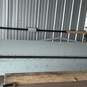 This machine is likely a manual or hydraulic sheet metal brake. It is used to bend sheet metal into precise angles and shapes, which is essential in creating roofing panels, trims, and other custom metal components for roofs. The robust design suggests it's capable of handling thicker or longer sheets of metal.