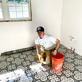 A Davie Mac Tile installer working on cleaning up grout from a decorative patterned floor with a Home Depot bucket.