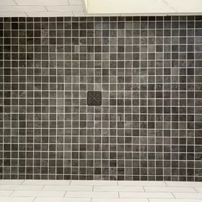 A shower floor with small square tiles and a centered black drain for symmetry.