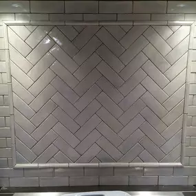 A herringbone tile backsplash installed with soft rustic handmade look-like tiles, illuminated by overhead lighting.