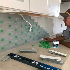 A backsplash installation in progress, featuring green tile spacers and glass subway tiles.