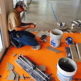 A craftsman working on a Schluter membrane, carefully cutting tiles with tools spread around.