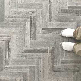 A floor featuring gray Limestone wood-look tiles laid in a herringbone pattern, with feet for scale.