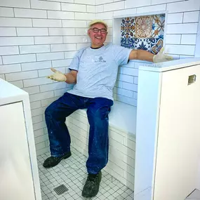 A tile craftsman sitting and smiling in a showroom filled with tile displays and sample boards.