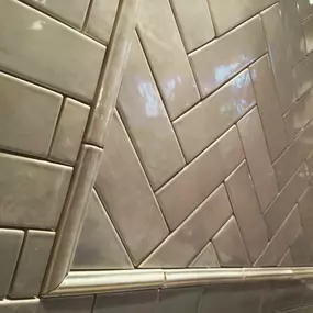 A close-up view of a herringbone pattern on gray subway tiles, before grouting.