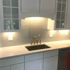 A bright kitchen with white cabinets and a glass subway tile backsplash, accented by under cabinet lighting.