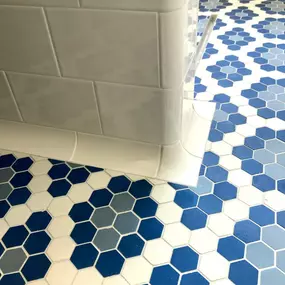 A close-up of a bathroom corner showcasing white subway tiles paired with bold blue hexagonal tiles by American Restoration Tiles on the floor.