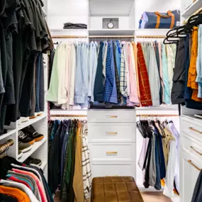 stunning white shaker closet with matte gold handles and rods. Back lighting really highlight the clothing.