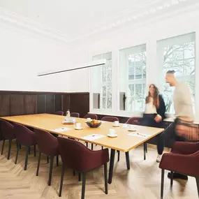 Ein stilvoller Meetingraum in der Alten Stadtkasse Oldenburg, ausgestattet mit einem großen Konferenztisch und eleganten Polsterstühlen. Helle Fensterfronten sorgen für eine angenehme Atmosphäre, während dunkle Holzelemente den historischen Charme des Raumes unterstreichen. Perfekt für Tagungen, Seminare und Geschäftstreffen mit bis zu 12 Personen.