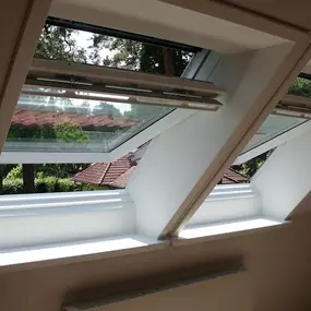 Ein moderner Raum mit zwei geöffneten Velux-Dachfenstern, die eine klare Aussicht auf grüne Bäume bieten und viel Tageslicht hereinlassen.