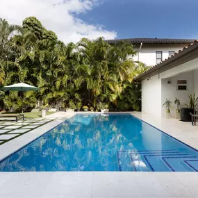 This inviting backyard retreat highlights Epic Watershapes' ability to transform any space into a private paradise. Our team designed and built this stunning pool, featuring a sleek rectangular shape, vibrant blue tiles, and integrated steps for easy access. The surrounding patio, with its modern travertine and lush green grass grid, creates a seamless transition between the pool and the home. Mature palm trees provide shade and privacy, enhancing the tranquil atmosphere. This project demonstrat