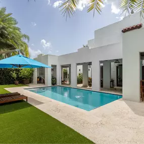 This tropical paradise showcases Epic Watershapes' ability to create a seamless blend of indoor-outdoor living. Our team designed and built this stunning pool area, featuring a refreshing rectangular pool with a tanning ledge and soothing water features. The expansive travertine patio extends from the home's covered outdoor living space, creating a unified and inviting entertainment area. Lush green grass surrounds the pool, providing a soft and comfortable space for lounging. Towering palm tree