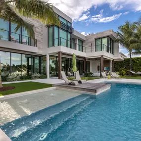 This modern outdoor haven showcases Epic Watershapes' ability to seamlessly integrate a pool into a contemporary architectural design. Our team constructed this stunning pool area, featuring a sleek rectangular pool with a spacious sun shelf and relaxing bubbler fountains. The pool's clean lines and minimalist aesthetic complement the home's sharp angles and expansive windows. A raised wooden deck provides a cozy space for lounging poolside, while the surrounding lush green lawn offers ample roo