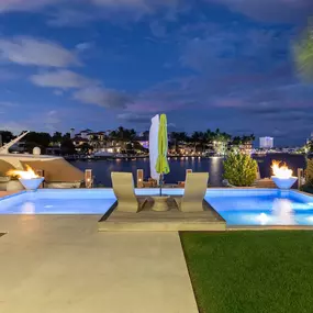 This luxurious waterfront escape showcases Epic Watershapes' dedication to creating sophisticated and inviting outdoor living spaces. Our team designed and built this stunning pool area, featuring a sleek rectangular pool with integrated fire bowls and submerged lighting that creates a mesmerizing ambiance at night. The expansive travertine patio offers ample space for lounging and entertaining, while the raised platform with lounge chairs provides a unique vantage point for enjoying the breatht