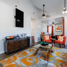 Vibrant and welcoming lounge featuring bold orange accents, plush seating, and modern décor. Includes a refreshment station, wall-mounted TV, and glass coffee table, creating a perfect space for residents to relax and socialize.