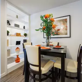 Elegant dining area featuring a dark wood table with cushioned chairs, accented by fresh floral décor and warm orange place settings. Built-in shelving adds a stylish touch while providing space for decorative pieces and storage.