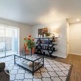 Bright and stylish living room featuring wood-style flooring, a cozy seating area, and a large sliding glass door that opens to a private patio. Accented with modern décor, a geometric rug, and a sleek coffee table for a comfortable yet contemporary feel.
