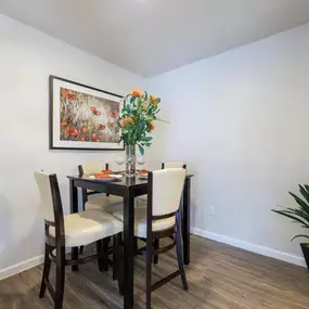 Elegant dining area in our 1-bedroom, 2-bedroom, and 3-bedroom apartment complex at The Brook on Bay Area. Features a dark wood table with cushioned chairs, bright floral centerpiece, and modern wall art, creating a perfect space for meals and gatherings.