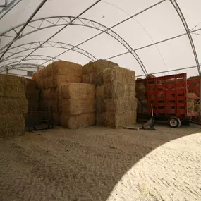 Interior of an arched fabric structure used for agricultural storage, showing stacked hay bales and farm equipment.