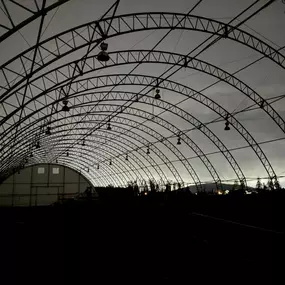 Interior silhouette of a Pilot Buildings arched structure at dusk or night, highlighting the steel frame and overhead lighting.