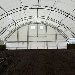 Interior view of the end wall of a Pilot Buildings arched structure, likely an arena, featuring high windows and solid kick walls.