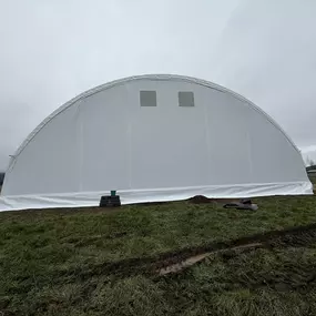 Exterior end view of a completed Pilot Buildings arched fabric structure featuring a white fabric end wall with two upper windows.