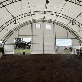 High-angle exterior view of a completed Pilot Buildings arched fabric structure situated on a rural property, showing the end wall with doors.