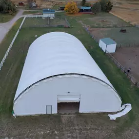 High-angle exterior view of a completed Pilot Buildings arched fabric structure situated on a rural property, showing the end wall with doors.