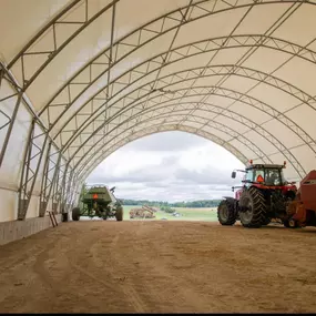 Spacious interior of a Pilot Buildings fabric structure used for storing large agricultural equipment, with an open end showing the outdoors.