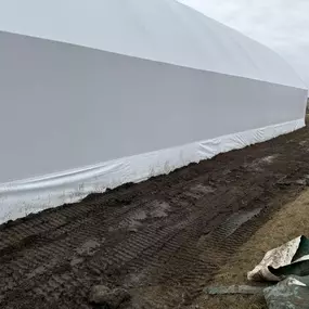 Close-up exterior view of the base of a Pilot Buildings white fabric structure, showing the wall meeting muddy, track-marked ground.
