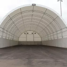 Interior perspective of a large, wide-span Pilot Buildings arched structure mounted on high concrete foundation walls, featuring a paved floor.