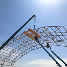 Installation of roof fabric panels onto the erected steel frame of a Pilot Buildings arched structure, using a crane and aerial lifts.