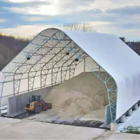 High-angle view of an open-ended Pilot Buildings arched structure, mounted on concrete piers, used as a salt storage facility with a wheel loader inside.