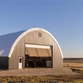 Exterior view of an arched building combining a white fabric roof with dark metal siding on the end and side walls, displaying logos for Northern Steel Buildings and Britespan.