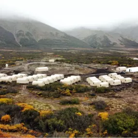Aerial view of a remote camp comprised of numerous small, identical Pilot Buildings arched fabric shelters arranged in rows within a rugged landscape.