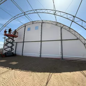 See the Pilot Buildings team in action during an arena re-cover. We install high-quality HDPE fabric, available in various colors, transforming older structures like this 27-year-old building with features like custom red end walls.